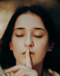why some people look more attractive even without makeup Close-up of a woman with closed eyes making a hush gesture with her finger on her lips, conveying silence.