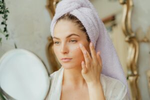 Morning VS Night Skin Care Routine what actually works Woman with head towel applying moisturizer in front of mirror indoors.
