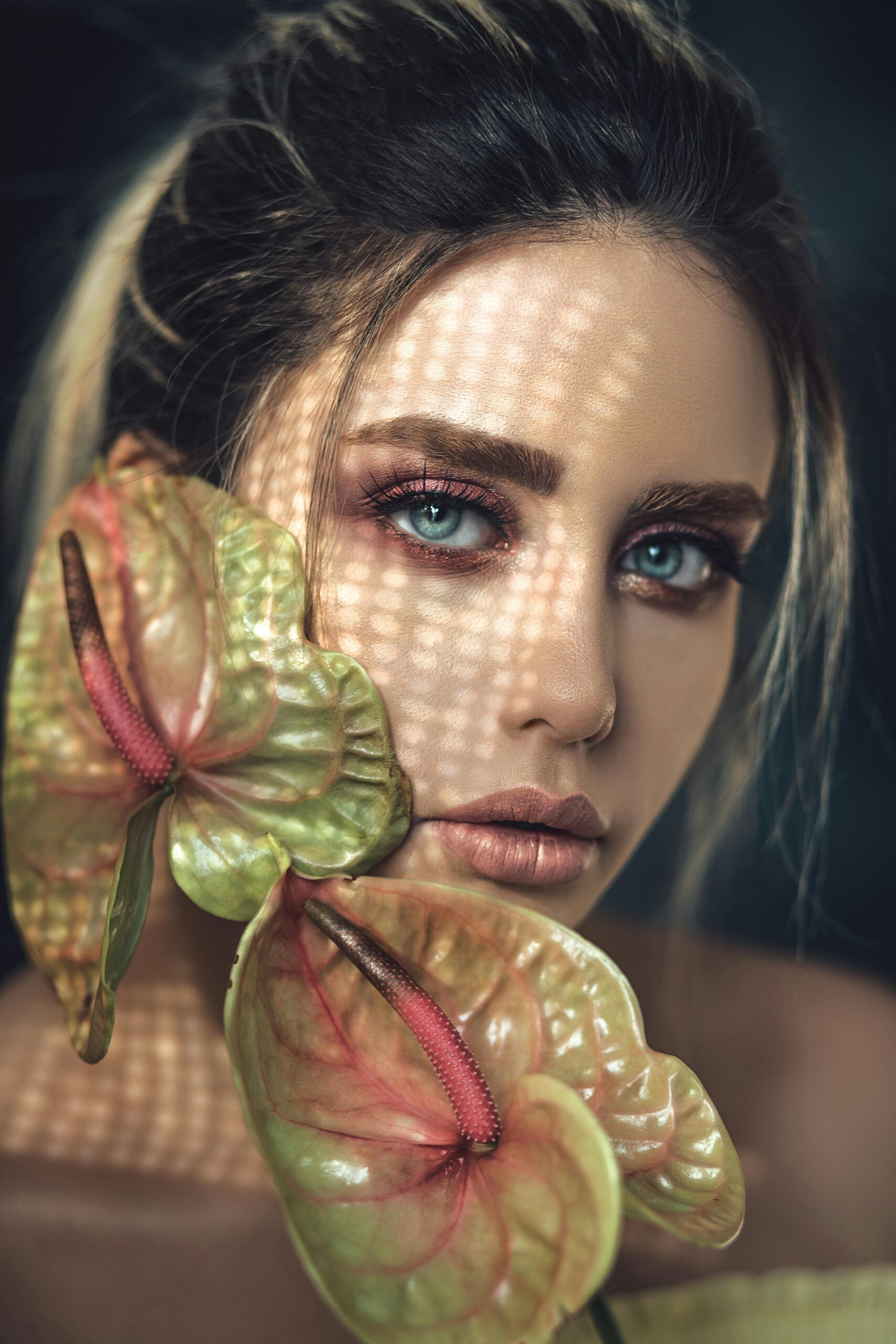 About Close-up portrait of a woman with vibrant makeup and anthurium flowers, featuring dramatic lighting.