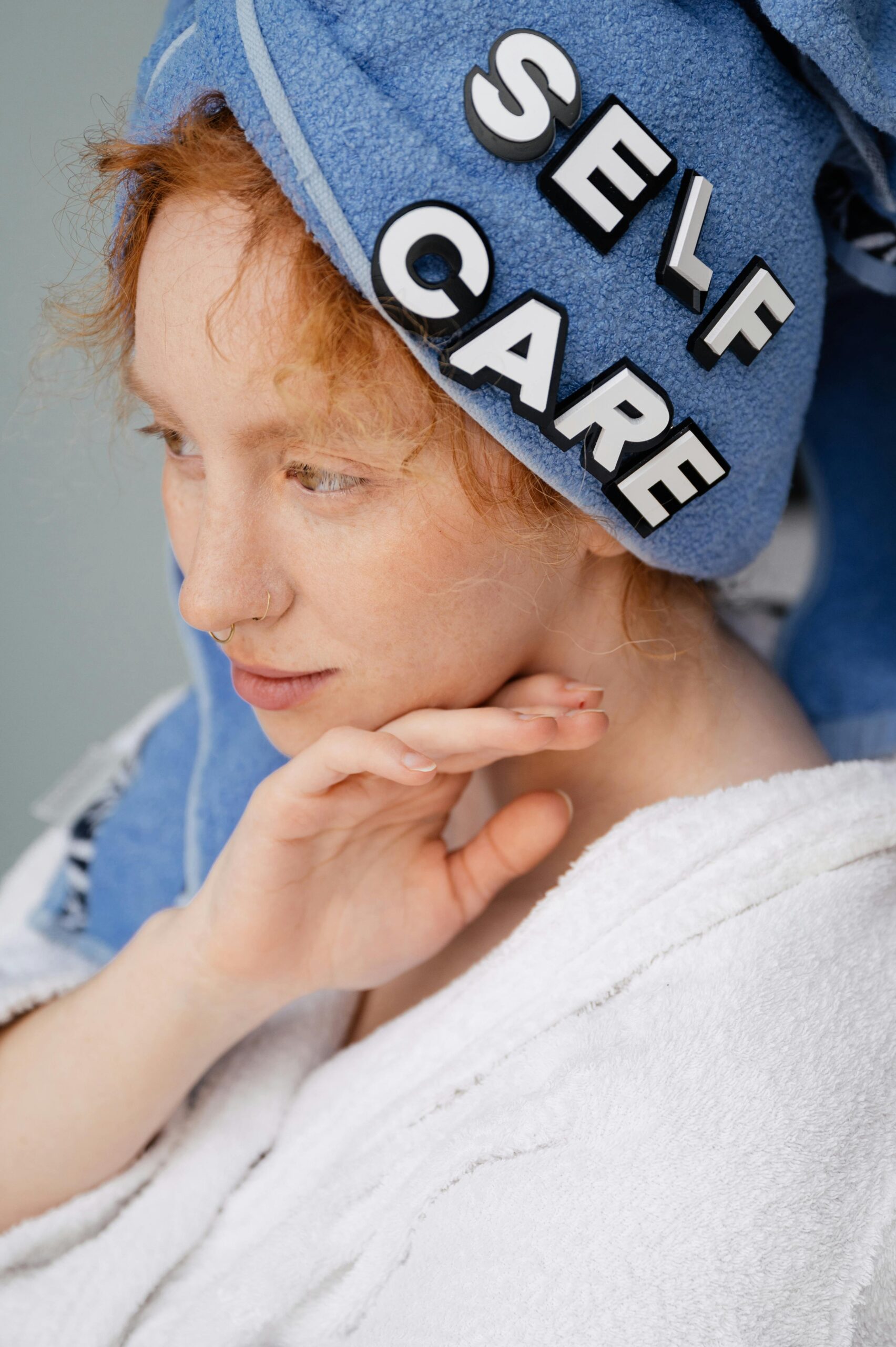 About A woman wearing a blue towel with 'self care' letters enjoys a peaceful moment indoors.